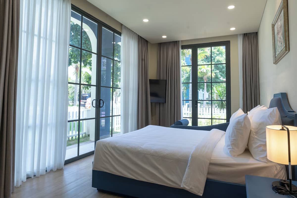 A modern hotel room with a large bed, a bedside table with a lamp, and a TV mounted on the wall.