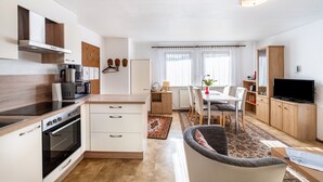 Cocina moderna con estufa, microondas y armarios, comedor con mesa y sillas, y un televisor en un mueble de madera.