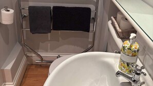 A bathroom with a white sink, a glass shelf above the toilet, and a towel rack with two towels.
