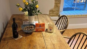 A wooden dining table with a bottle, a bowl of nuts, a box of matchmakers, and a vase of flowers.