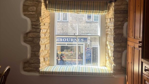A room with a stone wall, a window with a striped valance, and a wooden cabinet.