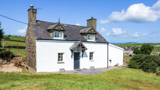 A white house with a stone foundation, two chimneys, and a slate roof.