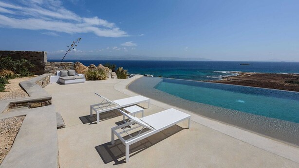 Un área lounge moderna al aire libre con mobiliario blanco, una piscina y vista al mar.