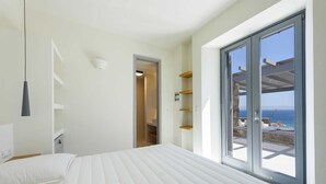 Un dormitorio con una cama, una puerta que da a un balcón y vista al mar.