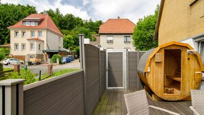 A wooden sauna structure, a wooden deck, and a gated entrance to a residential area. - Apartment 'Harzblick Am Waldesrand' with Mountain View, Private Terrace (and Sauna) (Hahausen)