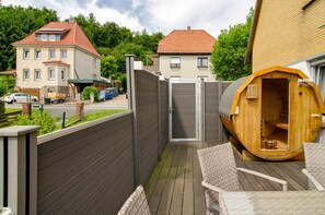 A wooden sauna structure, a wooden deck, and a gated entrance to a residential area. - Apartment 'Harzblick am Waldesrand' with Mountain View, Private Terrace & Sauna (Hahausen)
