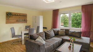 A living room with a sofa, chairs, a dining table, and a window with curtains.