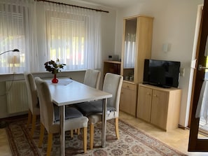 A room with a dining table, chairs, a TV, a cabinet, and a window with curtains. - Apartment 'Linde' with Shared Garden, Balcony and Wi-Fi (Endingen am Kaiserstuhl)