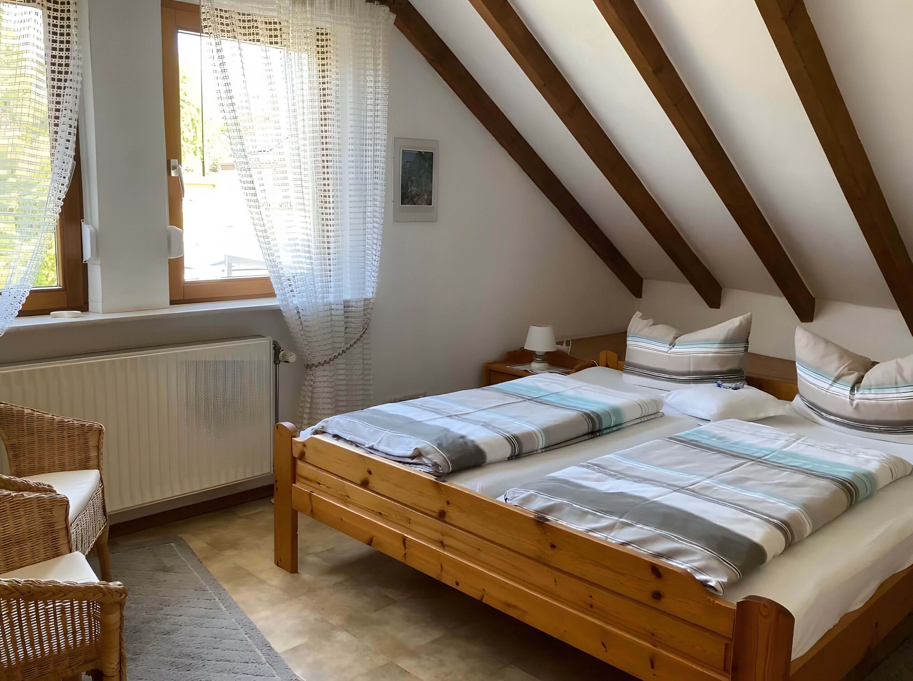 Un dormitorio con cama de madera, ventana con cortinas de encaje, radiador y mesita de noche con lámpara.