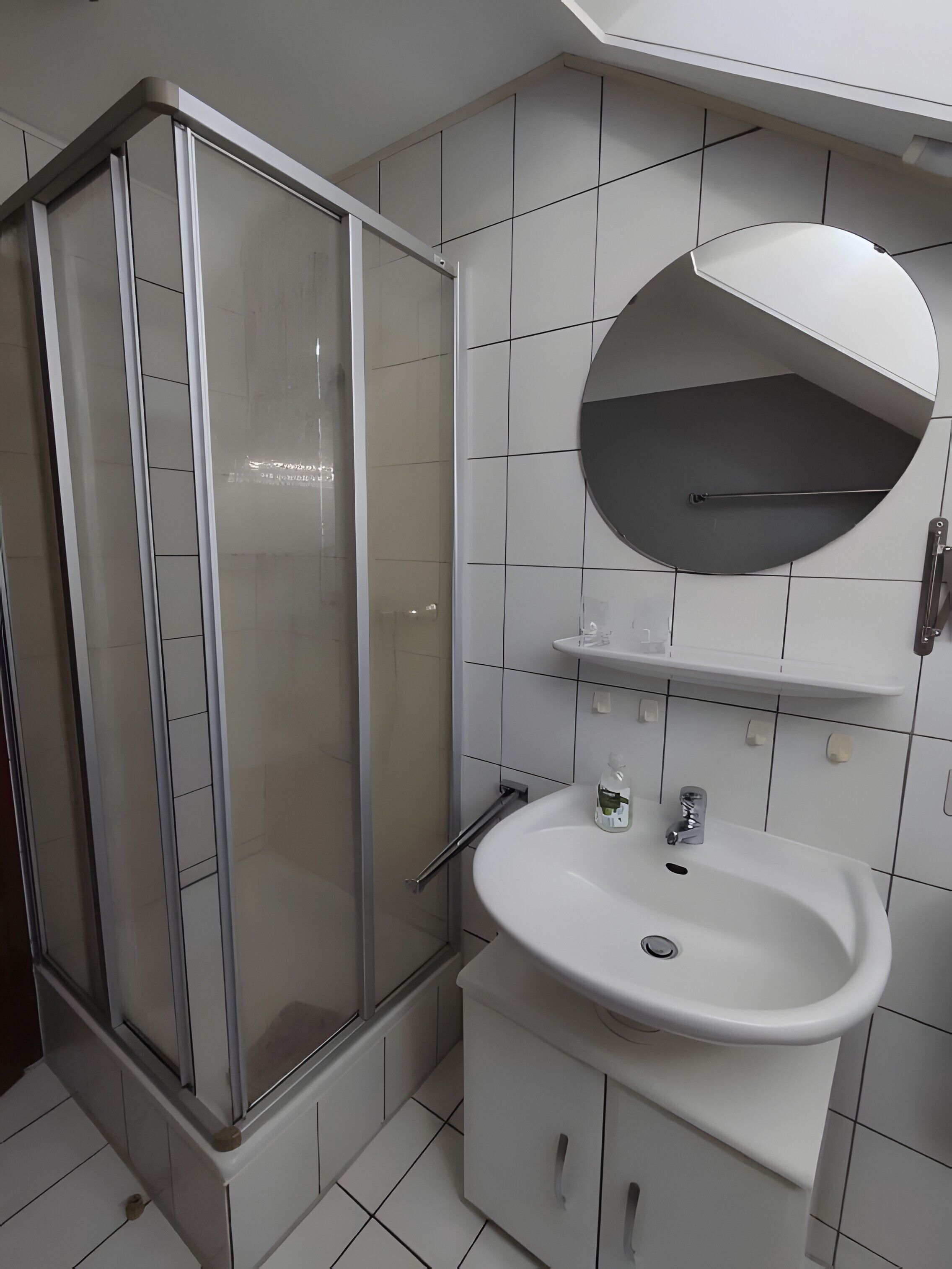 Ein Badezimmer mit Duschkabine aus Glas, einem weißen Waschbecken und einem Spiegel darüber.