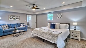A bedroom with a bed, a blue sofa, a small table, a nightstand, and a ceiling fan.