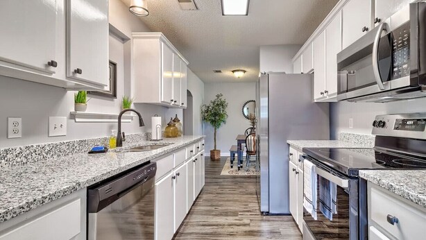 A modern kitchen with white cabinets, granite countertops, stainless steel appliances, and a wooden floor.