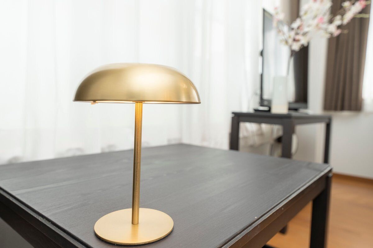 A modern table lamp with a gold base and a dome-shaped shade, placed on a dark wooden table.