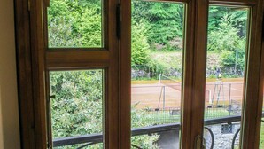 Una ventana con vistas a una cancha de tenis y follaje.