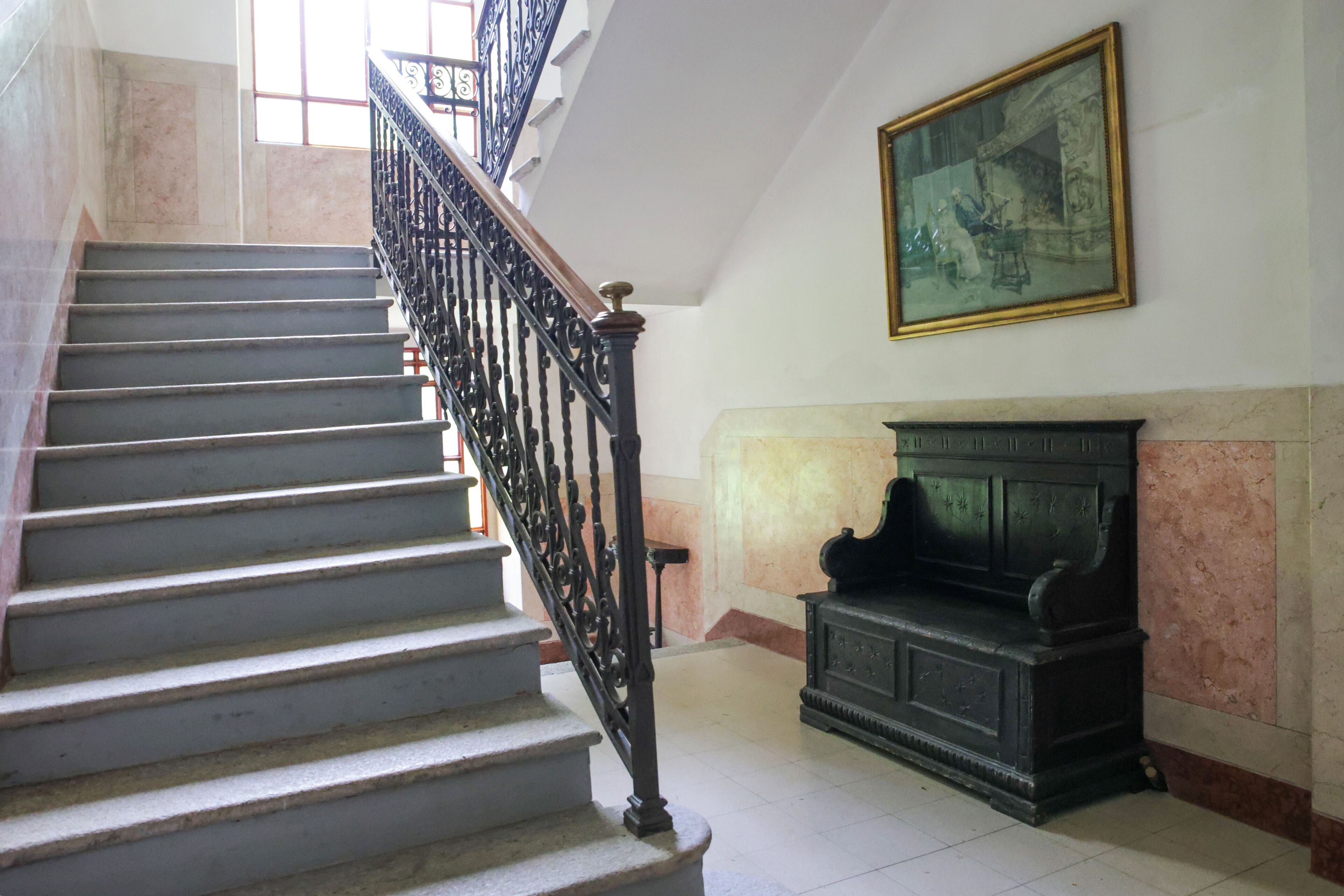 A staircase with a black iron railing, a marble wall, and a framed picture on the wall.