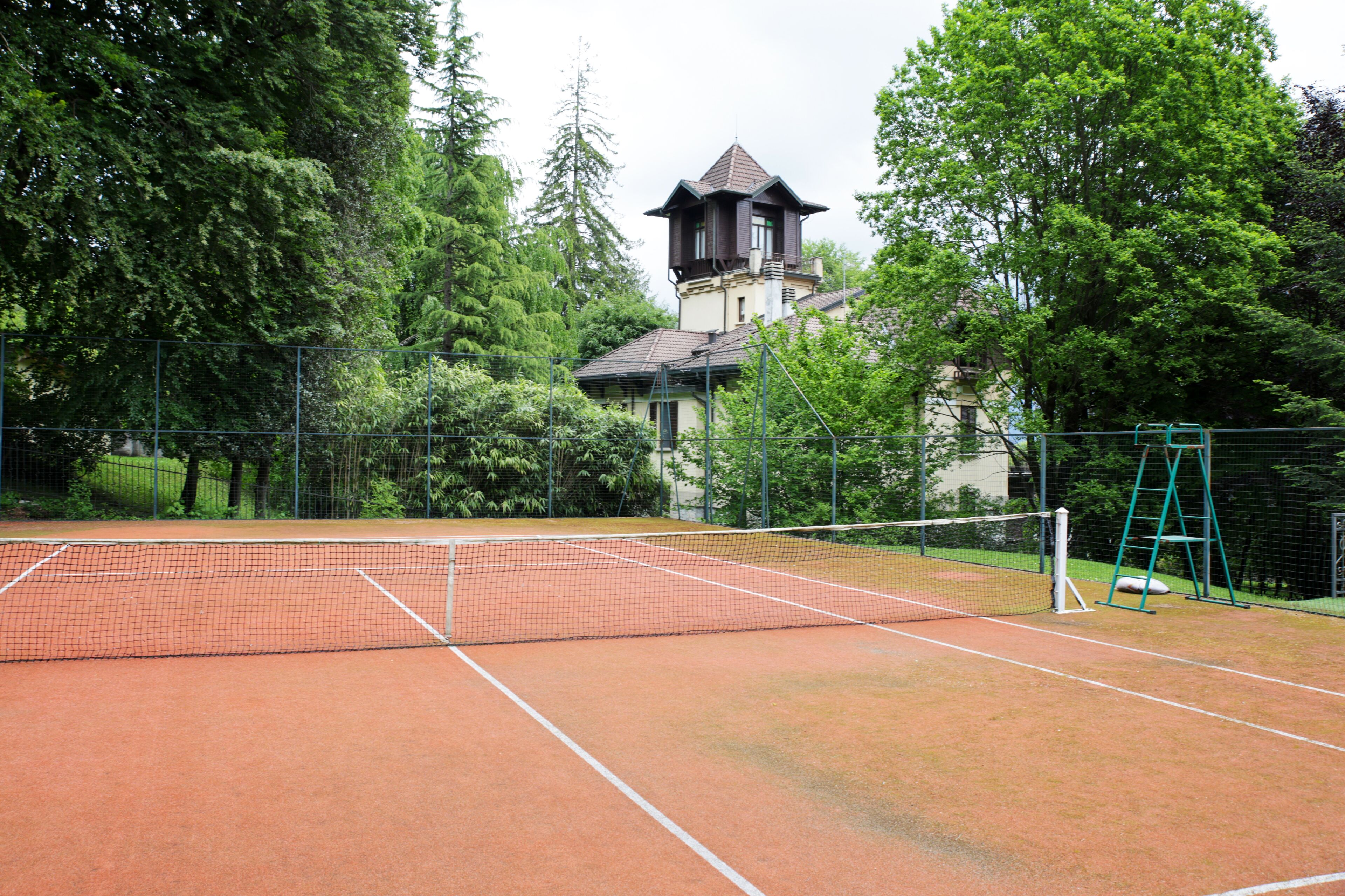 A tennis court with a net, surrounded by trees and a building with a tower.