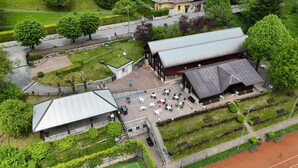 Vista aérea de un edificio con un amplio patio, mobiliario exterior y una cancha de tenis.