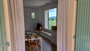 Ein Essbereich mit Tisch für zwei Personen, ein kleines Fenster mit Blick auf Grünflächen und eine Tür mit grünen Fensterläden.