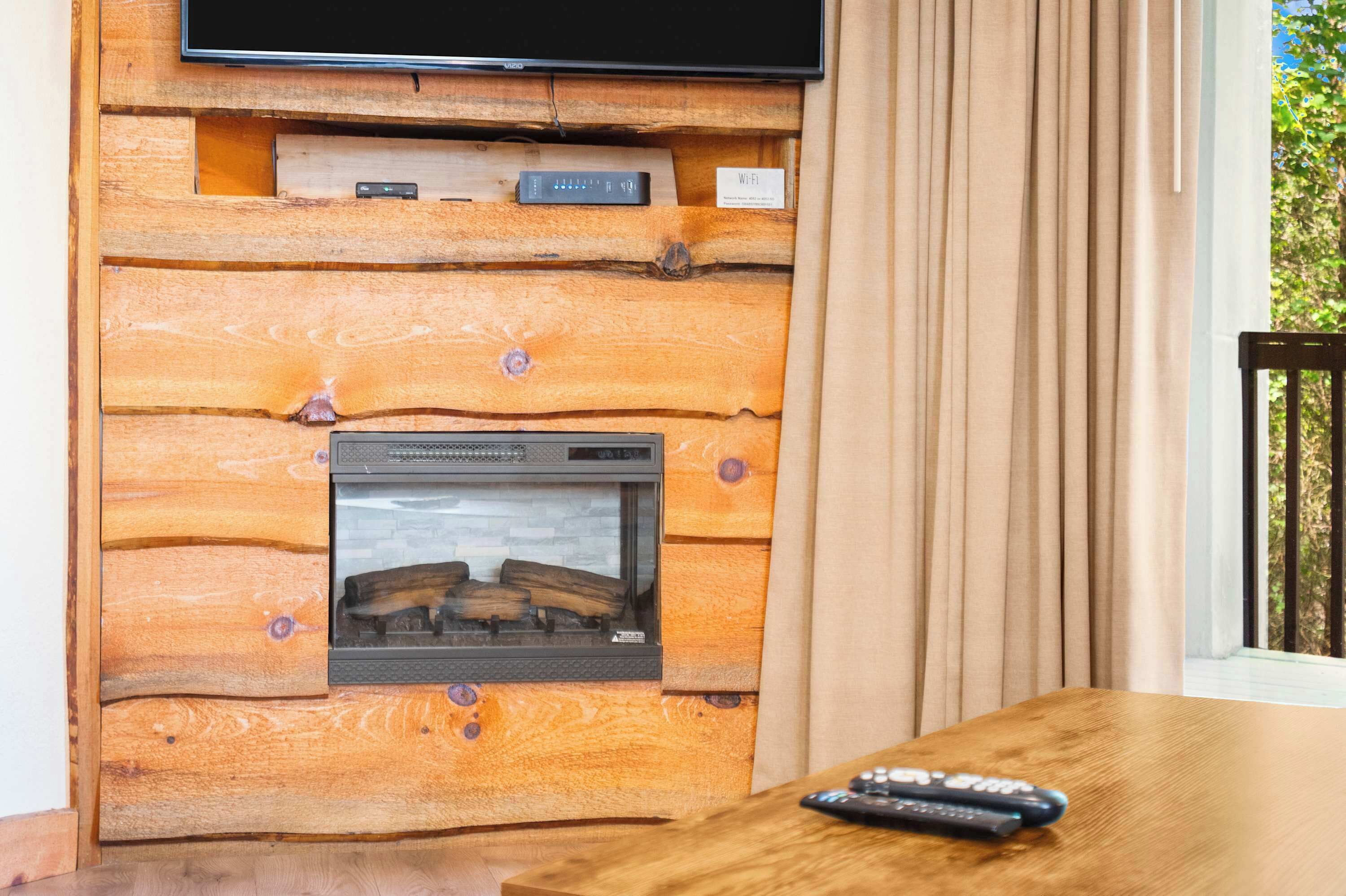 A wooden wall with a fireplace, a flat-screen TV, and a remote control on a wooden table.