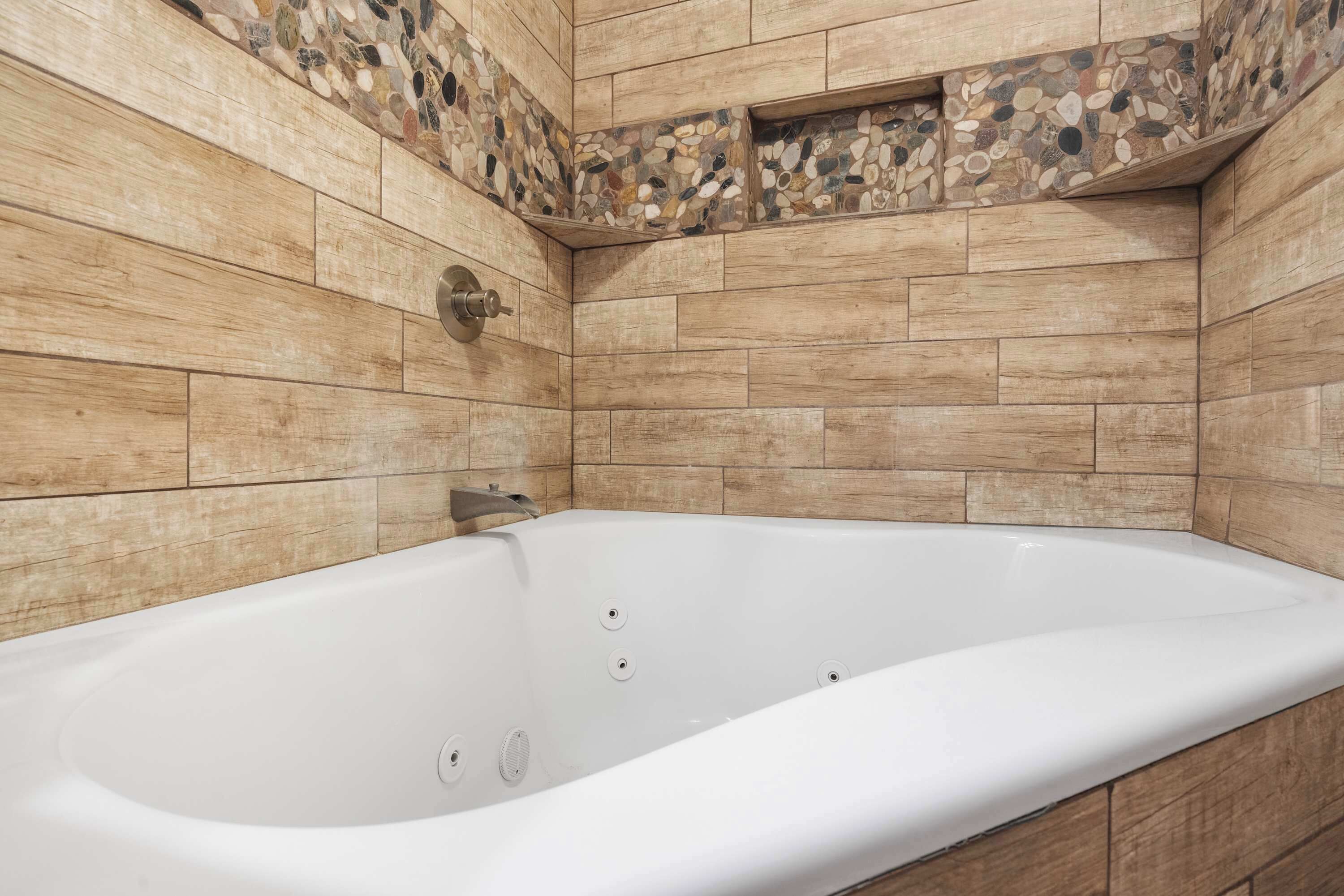A modern bathroom with a freestanding bathtub, tiled walls, and a pebble accent wall.