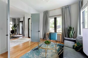Een moderne woonkamer met een grijze bank, een ronde salontafel en uitzicht op het groen door grote ramen.