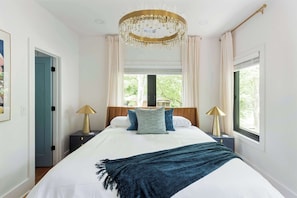 Een slaapkamer met een groot bed, twee nachtkastjes, een kroonluchter en een raam met gordijnen.