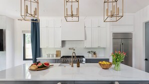 Eine moderne Küche mit weißen Schränken, einer großen Kochinsel mit Spüle und einem Edelstahlkühlschrank.