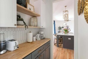 A modern kitchen with a wooden countertop, white cabinets, and a built-in coffee station.