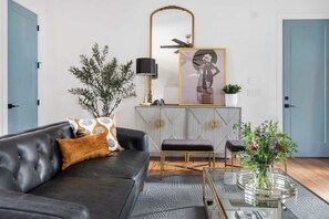 A modern living room with a dark leather sofa, a glass coffee table, and a decorative mirror.