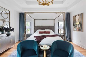 A modern bedroom with a four-poster bed, a side table, and two chairs.