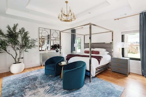 Een moderne slaapkamer met een hemelbed, twee fauteuils, een grote potplant en uitzicht op het omliggende landschap.