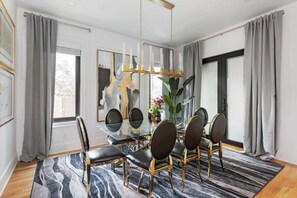 A dining area with a glass table, six chairs, a chandelier, and a large plant. - Cuppa Teal (Atlanta)