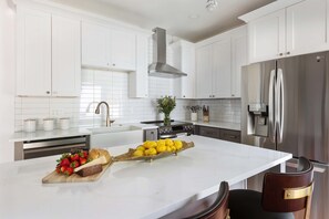 A modern kitchen with white cabinetry, stainless steel appliances, and a marble countertop. - Blue Burrow (Atlanta)