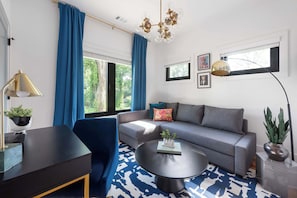 A modern living room with a grey sofa, blue curtains, a round coffee table, and a chandelier.
