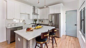 A modern kitchen with white cabinetry, stainless steel appliances, and a central island with bar stools. - Blue Burrow (Atlanta)