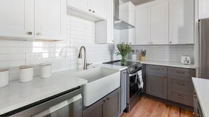 A modern kitchen with white cabinets, a stainless steel sink, and a built-in oven. - Blue Burrow (Atlanta)