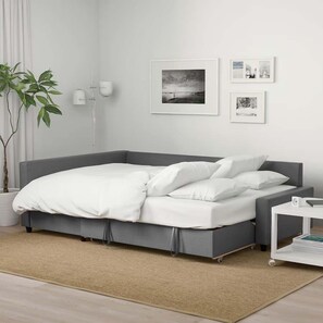 A modern bedroom with a grey sofa bed, a small bedside table with a lamp, and a large potted plant. - Blue Burrow (Atlanta)