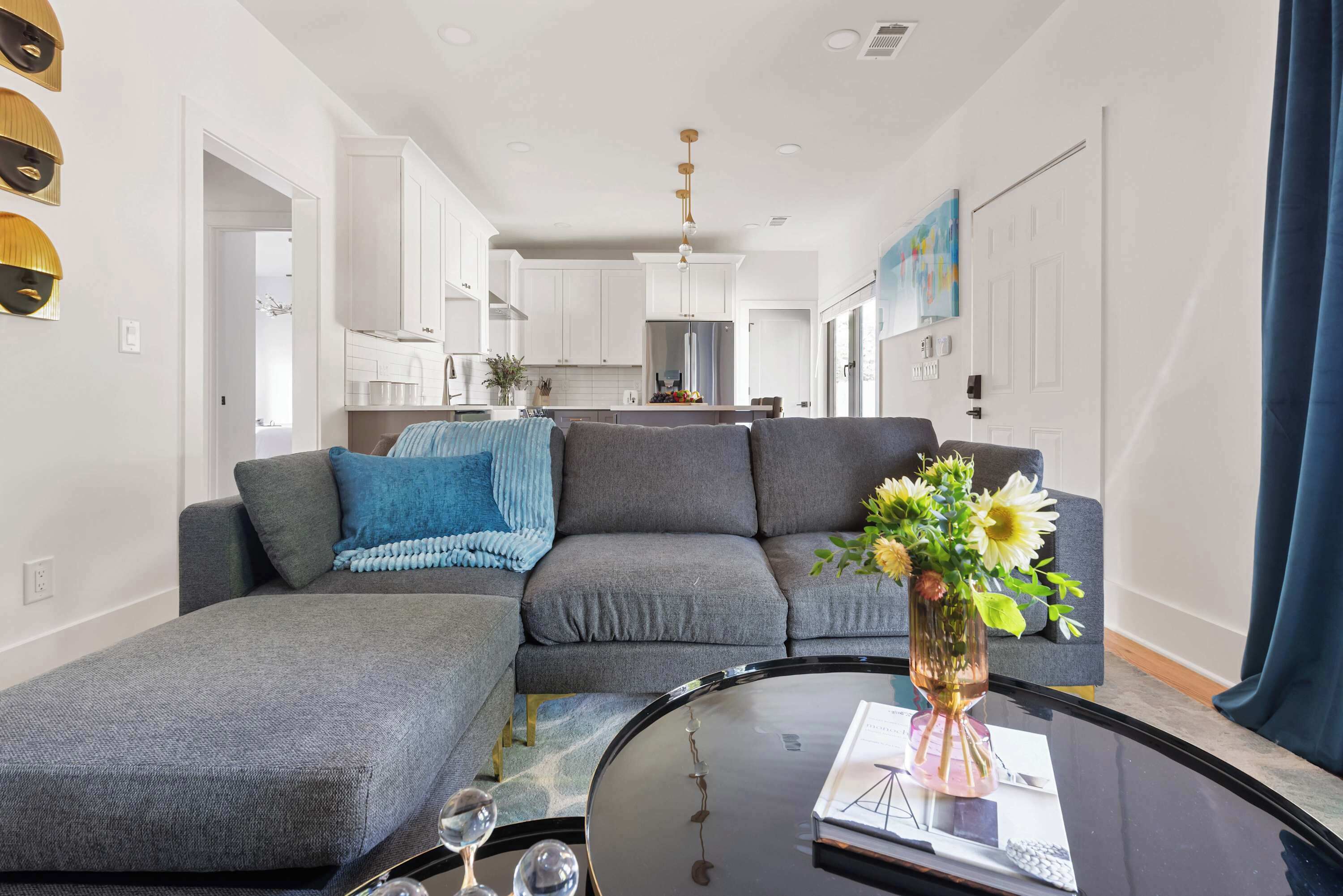 A modern living room with a grey sectional sofa, a glass coffee table, and a vase with flowers.