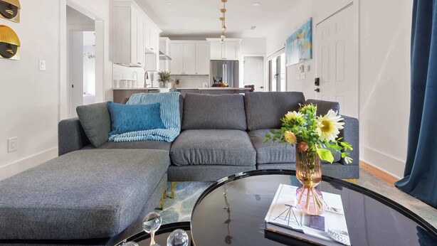 A modern living room with a grey sectional sofa, a glass coffee table, and a vase with flowers. - Blue Burrow (Atlanta)
