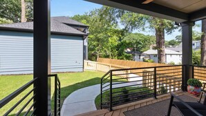 A covered porch with a wooden deck, a metal railing, and a view of a backyard with a lawn and a wooden fence. - Blue Burrow (Atlanta)