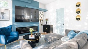 A modern living room with a blue sofa, a grey sectional, a black coffee table, and a flat-screen TV mounted on the wall. - Blue Burrow (Atlanta)
