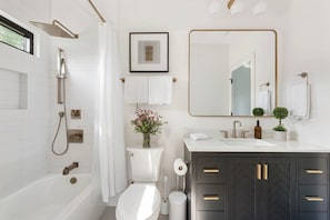A modern bathroom with a bathtub, toilet, shower, and vanity with a mirror and sink.
