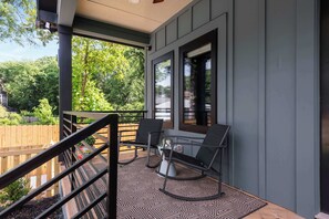 A covered outdoor seating area with a patterned floor, a wooden fence, and a view of a wooded area. - Blue Burrow (Atlanta)