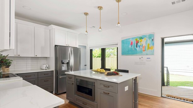 A modern kitchen with white cabinets, a stainless steel refrigerator, an oven, and a large island with a bowl of fruit. - Blue Burrow (Atlanta)