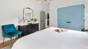 A bedroom with a large bed, a blue wardrobe, a black dresser, a teal chair, and a chandelier. - Blue Burrow (Atlanta)
