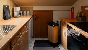 A kitchen with wooden cabinets, a skylight, a coffee maker, a trash bin, and a stove. - Apartment 'Kampenwand' with Mountain View, Balcony and Wi-Fi (Bad Endorf)