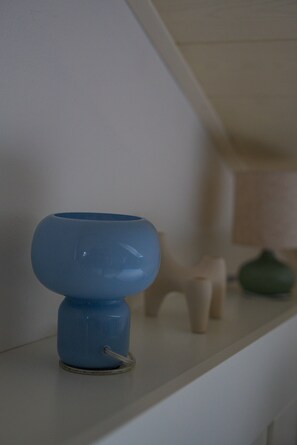 A blue object on a white shelf with a lamp and a small figurine in the background.