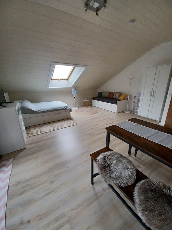 Une chambre de style loft avec une lucarne, un lit, un banc, une armoire et une petite table.