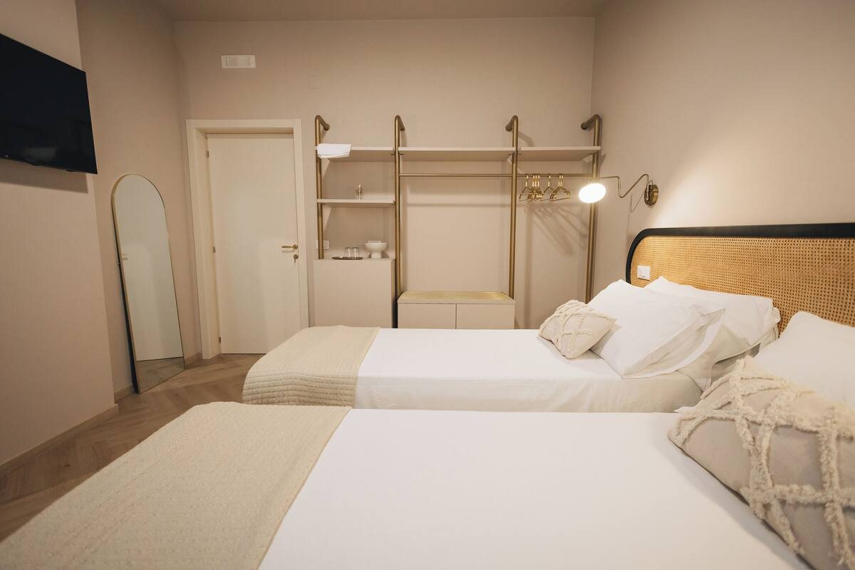 A bedroom with two beds, a wardrobe, a mirror, and a bedside table.