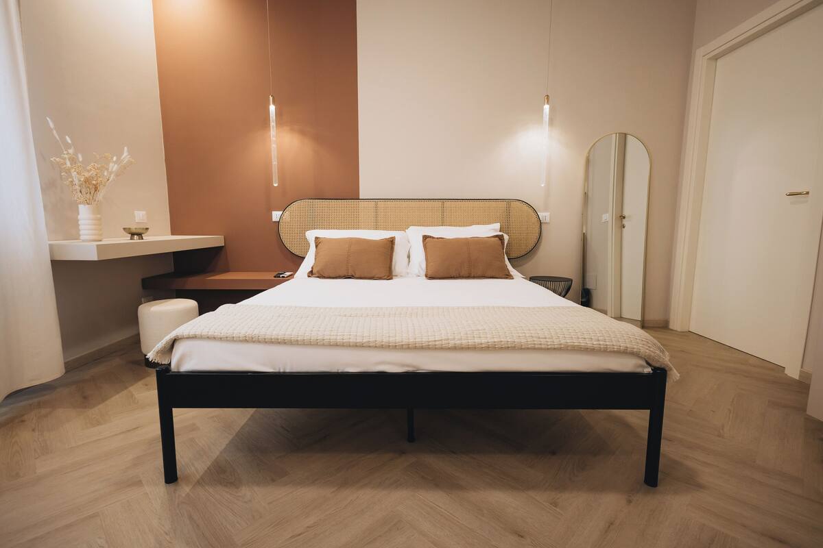 A modern bedroom with a bed, bedside tables, a mirror, and a small shelf with decorative items.
